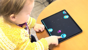 child in yellow sweater points at bubble on a tablet screen on a table