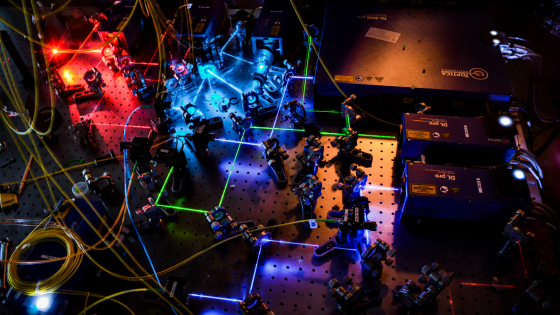 A bunch of machines lit with blue and red light with a maze of lasers running between them