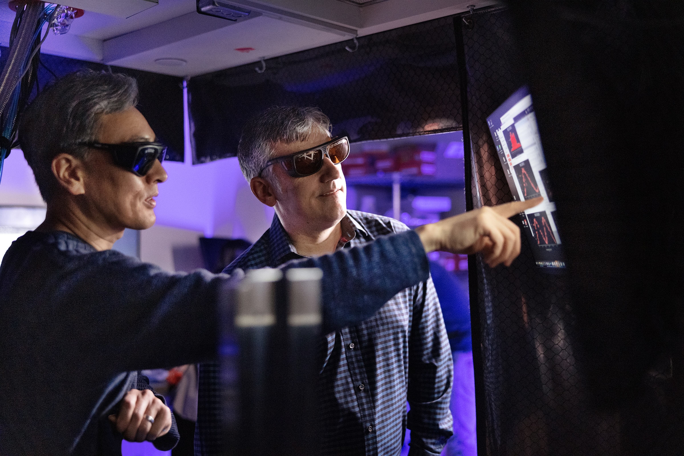 Photo of Jungsang Kim (right) and Chris Monroe (left), wearing protective sunglasses and looking at a computer screen.