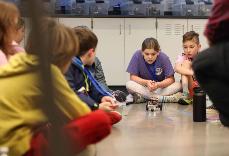 fourth grade students crowd around a small robot on the floor