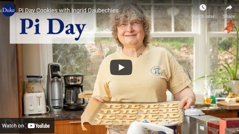 A woman standing with a tray full of Pi-shaped cookies in a kitchen