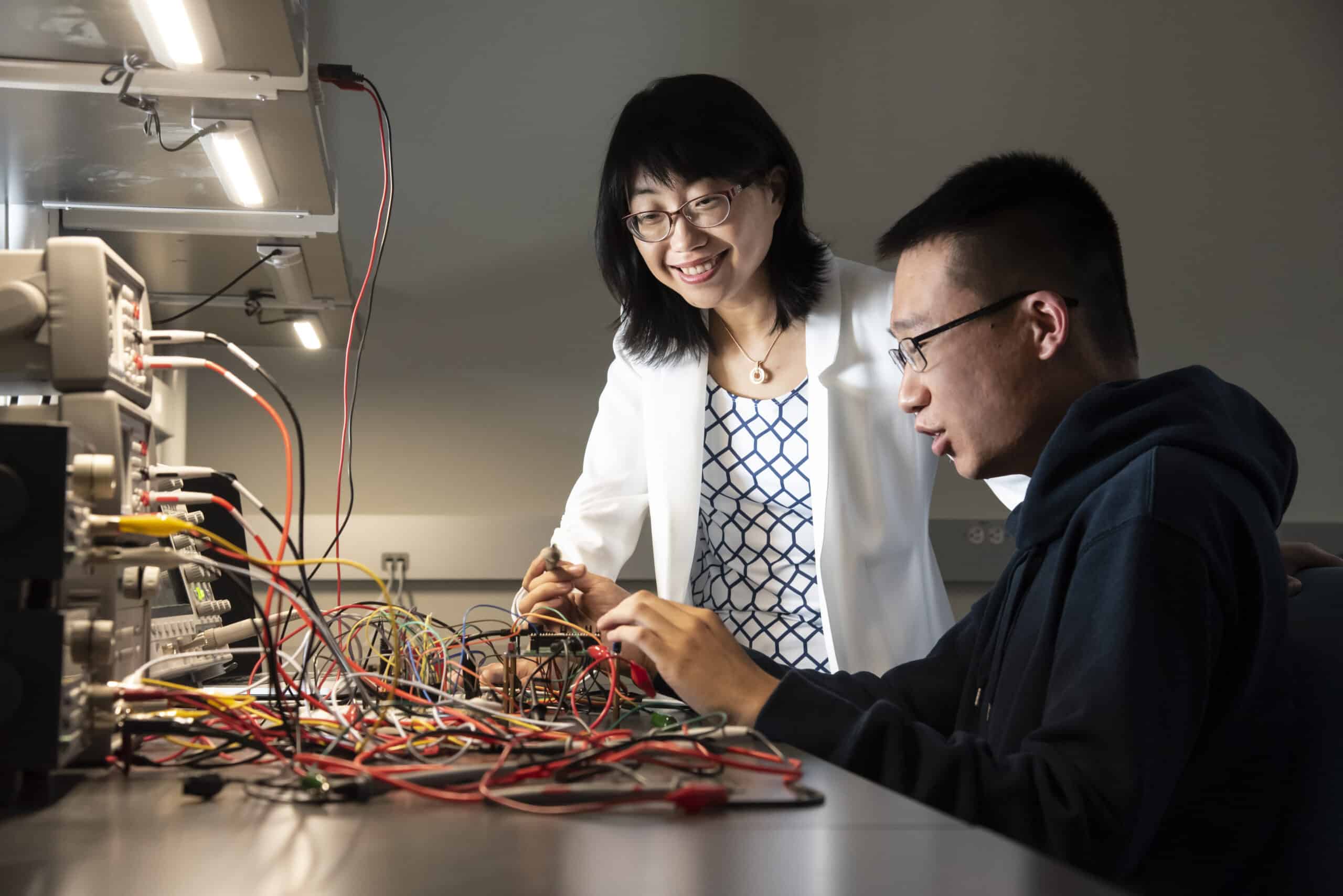 Helen Li and grad student working on electrical equipment in lab