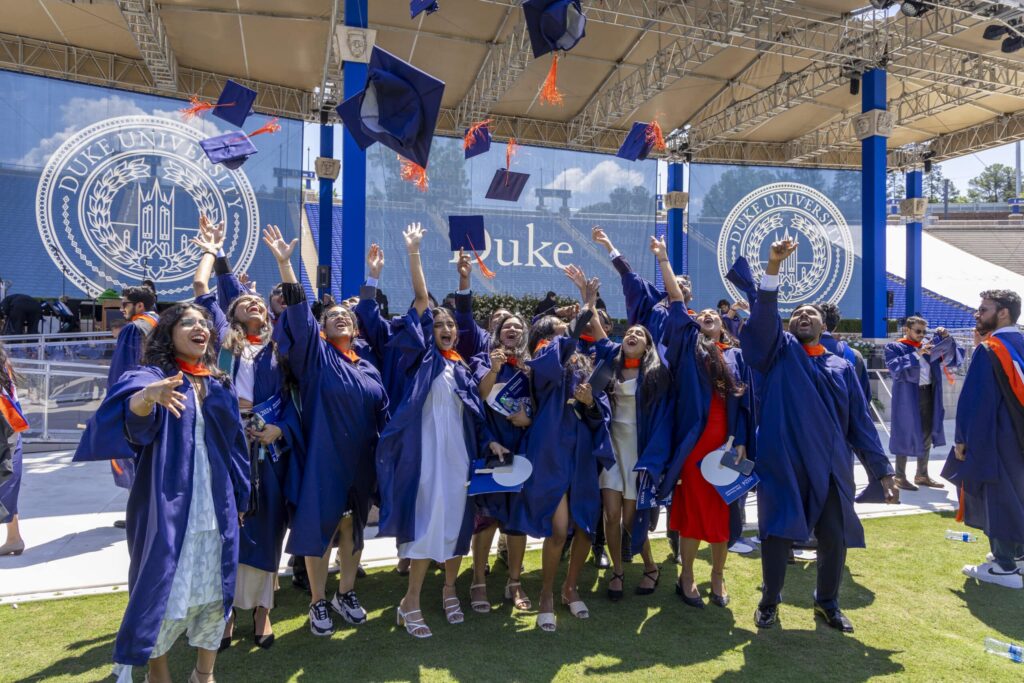 students toss caps at graduation in Wallace Wade Stadium