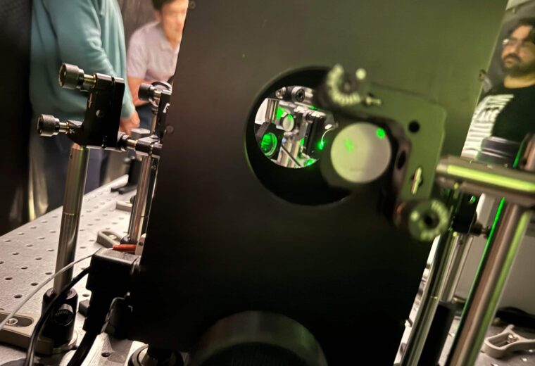 Peering through holes going through a rectangular black box looking at lenses and green lasers