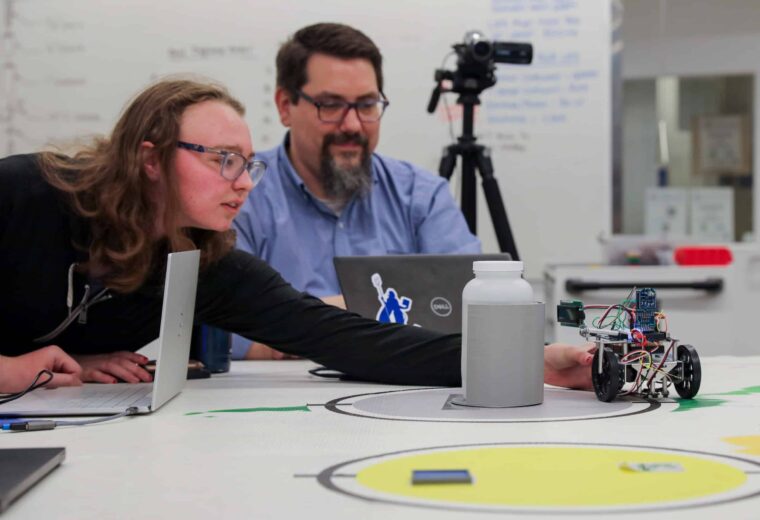 Adam Davidson watches as a student adjust a robot in the IDC.