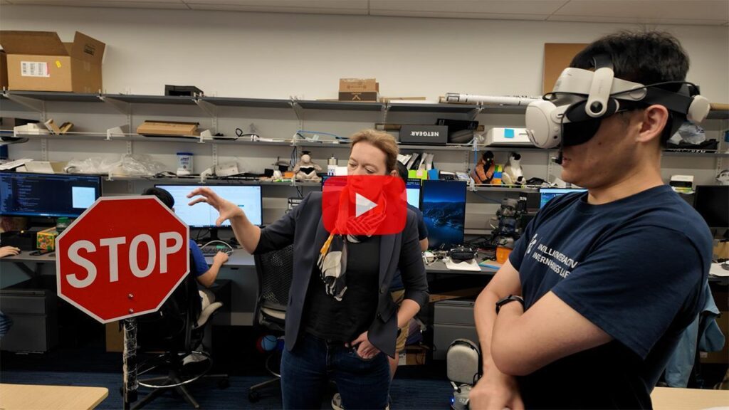 Maria Gorlatova points at a stop sign in her lab while a student wears an AR headset next to her.