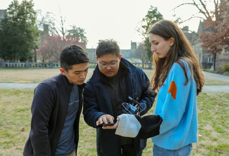 Tingjun Chen works looks at a device with two students on Duke's campus to measure wireless signals.